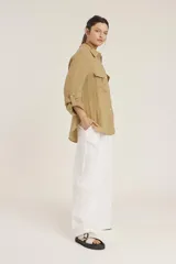 Camisa de lino color beige con cuello clásico, cierre frontal con botones, mangas largas con trabillas para enrollar y dos bolsillos con solapa en el pecho.