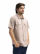 Camisa de manga corta color beige con cuello clásico, cierre frontal con botones, dos bolsillos con solapa abotonada en el pecho y corte recto. Ideal para actividades al aire libre.