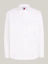 Camisa blanca de algodón con corte amplio, cuello inglés, bolsillo de parche en el pecho, logo de Tommy Jeans bordado en el bolsillo y detalles distintivos de la marca.