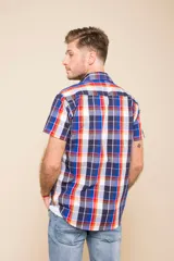 Camisa de manga corta con estampado a cuadros en tonos azul, rojo y blanco. Cierre con botones y tela ligera.