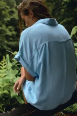 Mono corto de tela celeste, con cuello solapa, mangas cortas con dobladillo y cierre frontal con botones. Tiene un bolsillo de parche en el pecho.