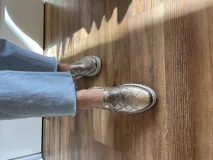 Zapatilla marrón de cuero con diseño entretejido, elástico lateral y suela blanca.