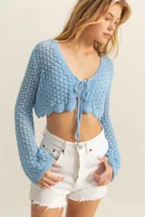 Top corto tejido crochet color celeste, con escote en V y mangas largas acampanadas. Se ata en el centro del busto con cordones del mismo tejido.
