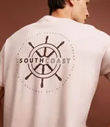 Remera de algodón color rosa claro, de corte clásico, con cuello redondo y manga corta. Presenta un pequeño estampado de un timón en el pecho y un estampado con letras en la espalda.