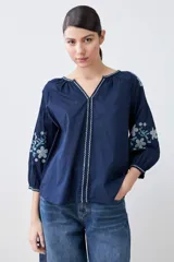 Blusa blanca de estilo boho con bordados de flores en amarillo y azul en mangas y escote.