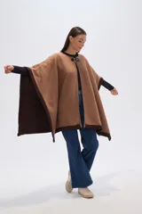 Poncho de tejido grueso color camel, con bordes y mangas en color marrón oscuro. Cierre frontal con broche rectangular negro.