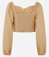 Blusa cropped color beige con escote corazón, mangas largas abullonadas con puños elásticos, botones frontales y detalle de volados en el ruedo.