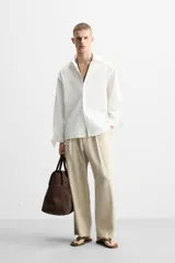 Camisa de algodón color blanco hueso, de corte relajado (relaxed fit), con cuello solapa y manga larga terminada en puño con botón. Cierre frontal con botonadura.