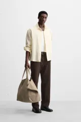 Camisa color crema de corte relaxed fit, confeccionada en tejido con mezcla de viscosa. Tiene cuello solapa, manga larga con puños abotonados, bolsillo de parche en el pecho y cierre frontal con botones.