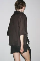Camisa marrón de corte recto, con cuello solapa, manga corta y cierre frontal con botones.