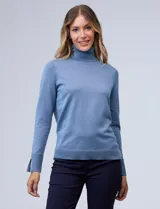 Polera de punto fino marca Nienty, color blanco, con cuello alto volcado y mangas largas con detalle de tajo en los puños.