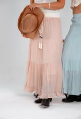 Pollera larga de color rosa pálido, con corte en capas y cintura elastizada. Incluye lazo fino del mismo material.