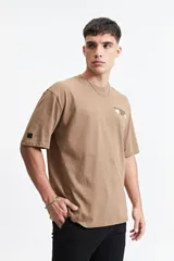 Remera color café de corte oversize con cuello redondo y mangas cortas. Estampado en la espalda con la frase "Stay Original Forever" y varios diseños gráficos.