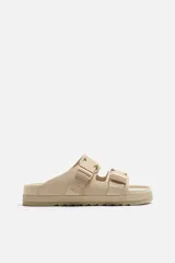 Sandalias planas color beige con doble tira ancha en el empeine y cierre con hebilla.