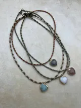 Collar de múltiples hebras con cuentas pequeñas de tonos tierra, rojo y azul, y dijes colgantes en forma de corazón con piedras semipreciosas engarzadas en metal dorado.