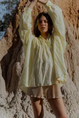 Camisa amarilla de algodón, corte suelto y largo asimétrico, más larga atrás que adelante. Tiene mangas largas amplias.