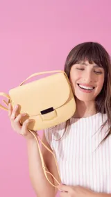 Bandolera de símil cuero color amarillo claro, con tapa y presilla. Tiene una correa extensible y un broche metálico rectangular en color negro.