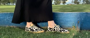 Zapatillas bajas con estampado animal print de vaca en blanco y negro, con cordones marrones y suela color caramelo.