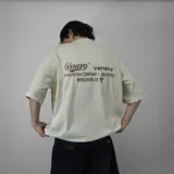 Remera beige claro de algodón, corte oversize, con estampado en la espalda que incluye la inscripción "Venefo Industries Company" y otros textos.