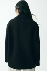 Abrigo corto negro de cuello solapa y manga larga. Tiene bolsillos de vivo en el delantero y cierre frontal con botones.