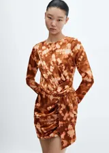 Vestido corto de poliéster con estampado tie-dye en tonos marrones y beige. Presenta cuello redondo, mangas largas, diseño cruzado con drapeado en la cintura y cierre de botón en la parte posterior.
