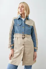 Trench largo color beige con secciones en denim azul, cuello camisero, cierre frontal con botones y bolsillos con solapa en el pecho.