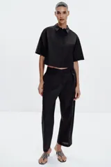 Camisa negra de popelín con cuello solapa y manga ancha por debajo del codo. Detalle de pinzas en la espalda y cierre frontal con botones ocultos por solapa.