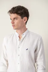 Camisa de lino blanca con cuello mao, corte slim fit y manga larga. Presenta un pequeño logo bordado de un pájaro en el pecho.