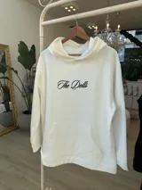 Hoodie negro de corte oversize, con capucha, bolsillo frontal y estampado blanco en la espalda con la inscripción "The Dolls The Dolls VIP CLUB".