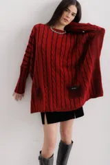 Sweater tejido de punto color fucsia con diseño de trenzas verticales en color naranja. Tiene cuello redondo y dos bolsillos frontales.