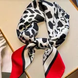 Pañuelo cuadrado de seda con estampado de manchas tipo dálmata en blanco y negro, con borde rojo y línea negra.