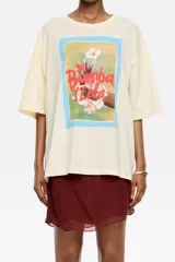 Camiseta color crema de algodón con estampado de un cuadro con borde celeste, con una mano sosteniendo una flor y el texto "Bimba y Lola".