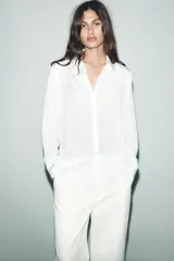 Camisa blanca de lyocell con cuello solapa, manga larga y bajo asimétrico. Cierre frontal con botones.