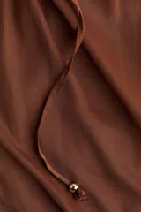 Pantalón palazzo color marrón con cintura elástica y cordón ajustable con cuentas decorativas. Tiene bolsillos laterales discretos.