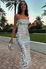 Vestido largo blanco tipo tubo cubierto de lentejuelas tornasoladas y plateadas, con tirantes finos y cierre en la espalda.