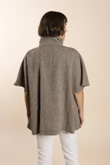 Capa acampanada color beige con manga corta, cierre metálico a la vista, cuello recto, bolsillos con tapa y terminaciones envivadas. Confeccionada en lana fina sin teñir, diseñada exclusivamente por Don Baez.