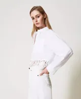 Camisa blanca de popelina de algodón con corte boxy y encaje macramé en el bajo. Presenta cuello clásico, manga larga con sisa caída, puños con abertura y botones, cierre con botones, bolsillos aplicados en la parte delantera y placa con logotipo Oval T en la parte trasera.