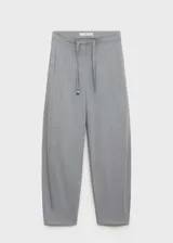 Pantalón gris de tiro medio y corte ancho, con bolsillos laterales, cierre oculto con botón, gancho y cremallera, y forro interior.