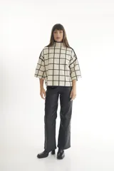 Sweater color crema con cuello alto y mangas cortas anchas, con diseño de cuadros negros.