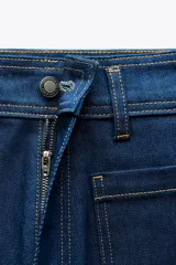 Pantalón de jean de tiro alto color negro con pierna ancha, bolsillos delanteros y traseros, y cierre frontal con cremallera y botón metálico.