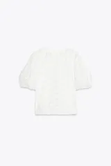 Camiseta blanca de cuello redondo y manga corta abullonada con elástico. Detalle de bordados perforados a tono.