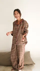 Conjunto de pijama de dos piezas color marrón con estampado a cuadros blancos y ribetes rosas. Incluye camisa de manga larga con cuello y botones, y pantalón largo de corte recto.
