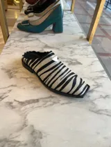 Zueco de cuero genuino con estampado animal print de cebra, punta cuadrada y detalle metálico lateral. Cuenta con suela de caucho y diseño destalonado.