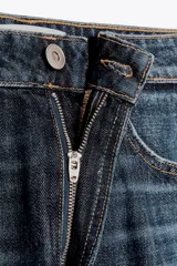 Pantalón de jean azul oscuro, tiro medio, corte amplio tipo baggy balloon con costuras torcidas y cinco bolsillos. Cierre frontal con cremallera y botón metálico.