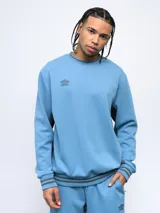 Buzo celeste de corte clásico con logo Umbro bordado en el pecho. Presenta cortes y cambio de color en las mangas, y ribete con rayas grises en cuello, puños y cintura.