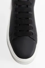 Zapatillas negras de cuero sintético con cordones negros y suela gruesa blanca.