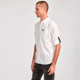 Camisa de popelina verde con cuello abotonado, cierre frontal con botones, bolsillo de parche en el pecho izquierdo, mangas largas con trabillas para enrollar y dobladillo camisero.