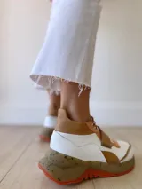 Zapatillas deportivas blancas con detalles en cuero color salmón y suela gruesa con detalles en naranja.