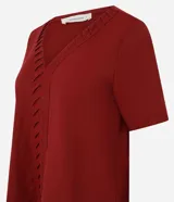 Blusa de manga corta color rojo oscuro (terracota/vino) con escote en V y detalle de pliegues verticales en el centro del frente.