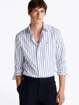Camisa de popelín de puro algodón a rayas verticales blancas y celestes con logo de Tommy Hilfiger bordado en el pecho. Cuenta con cuello abotonado, mangas largas con puños abotonados y corte regular.